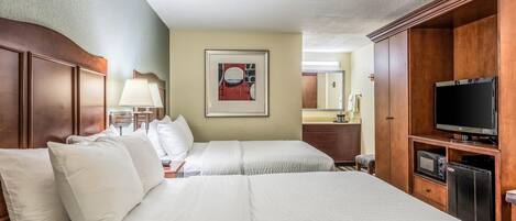 A hotel room with two beds, a television, a microwave, and a framed artwork on the wall.
