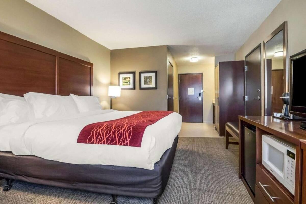 A hotel room with a bed, a desk with a television, a microwave, and a door leading to another room.