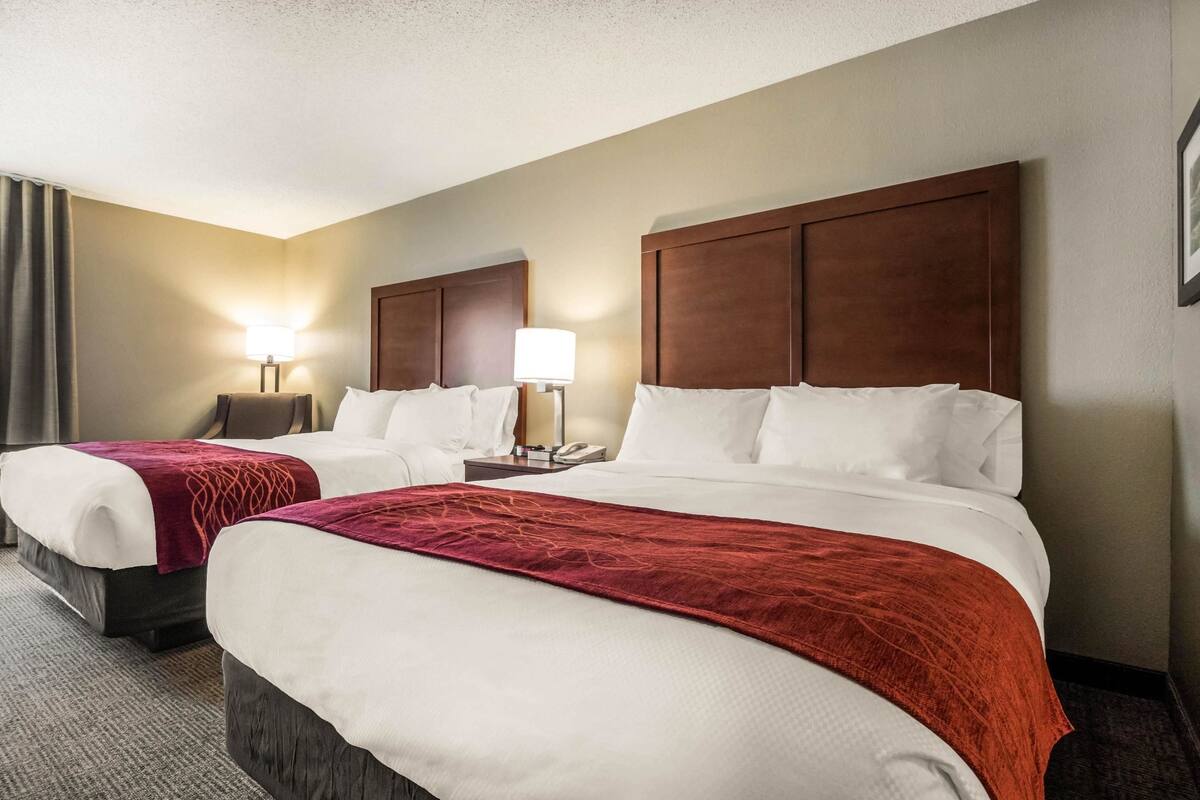 A hotel room with two beds, each with white linens and a red throw blanket. There are bedside tables with lamps and a telephone.
