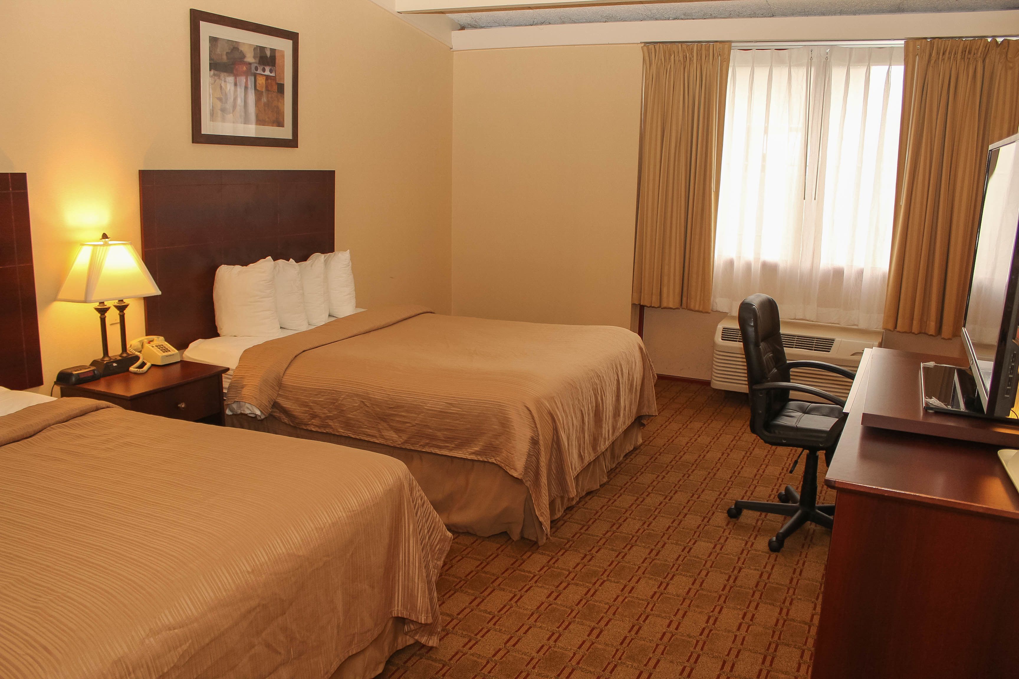 Une chambre d’hôtel avec deux lits, un bureau, une chaise, un téléphone et une fenêtre avec des rideaux.