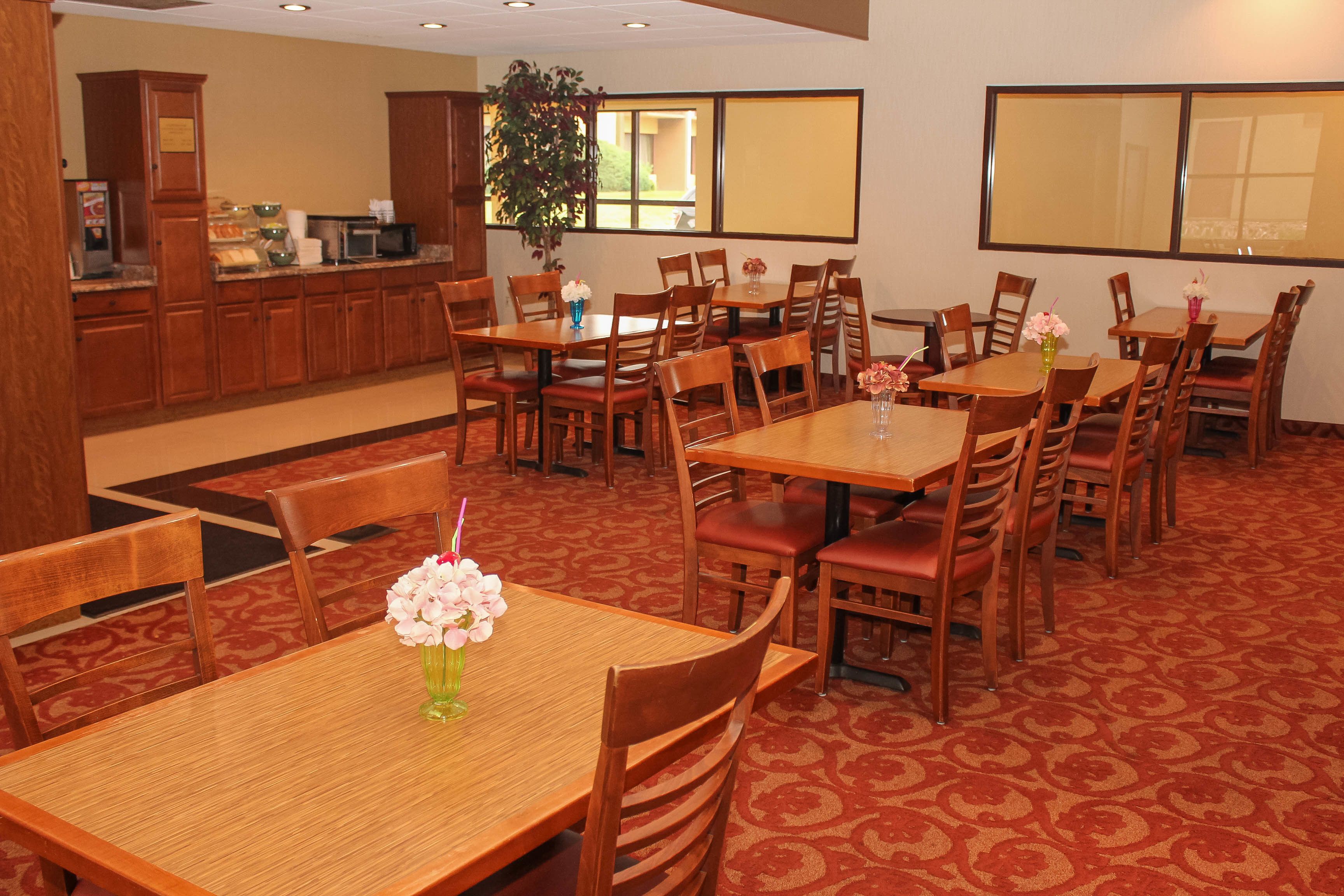 Un comedor de hotel con varias mesas y sillas de madera, una barra de buffet y un amplio ventanal que proporciona luz natural.
