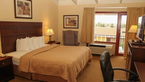 Una habitación de hotel con una cama grande, un escritorio con computadora, una silla, una ventana con cortinas y un cuadro en la pared.