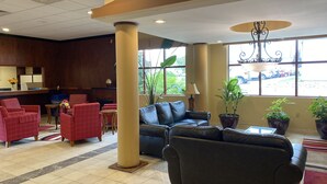 Un hall con mostrador de recepción, sillones rojos, un sofá de cuero negro y grandes ventanales con vistas al exterior.