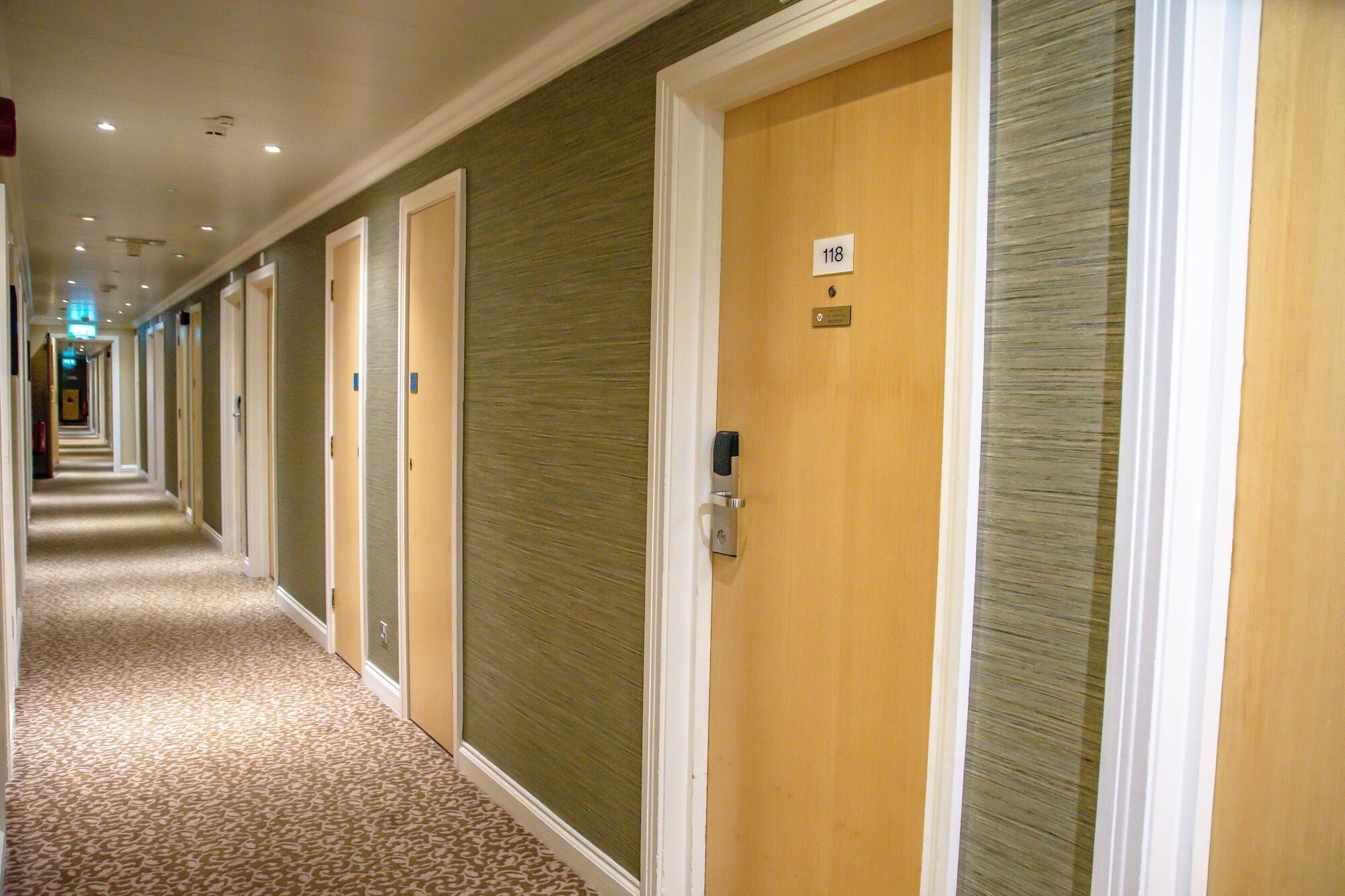Ein Hotelkorridor mit Türen mit den Nummern 118, Teppichböden und einheitlichem Wanddesign.