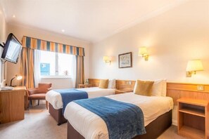 A hotel room with two beds, a desk, a chair, a TV, and a window with curtains.