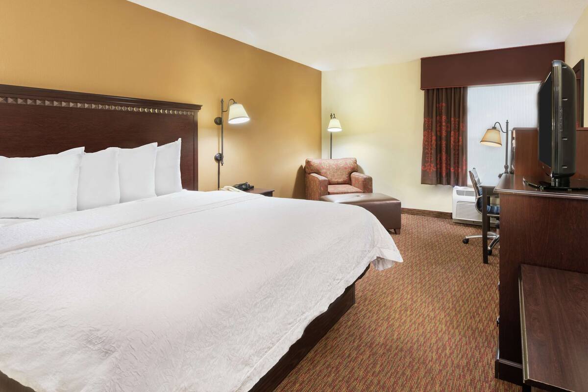 A hotel room with a large bed, a desk with a computer, a chair, and two wall-mounted lamps.