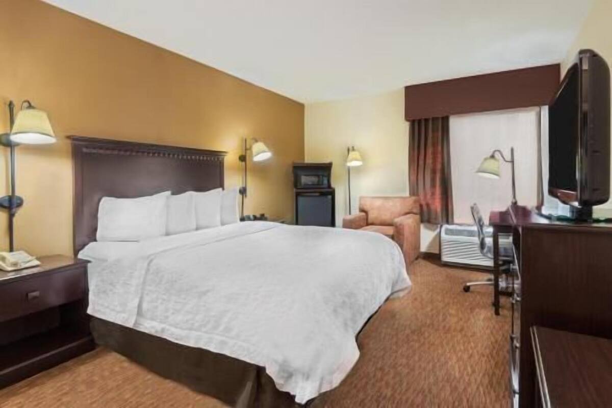 A hotel room with a large bed, two bedside lamps, a desk with a computer, a chair, and a television.