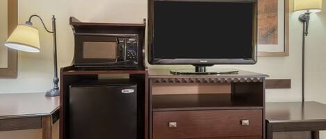 A compact minibar with a refrigerator, microwave, and a flat-screen TV on a wooden cabinet.