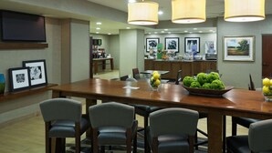 A spacious dining area with a long wooden table, multiple chairs, and a central fruit bowl. - Hampton Inn Charlotte - University Place (Charlotte)