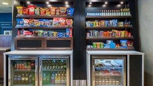 A snack and beverage display area with shelves stocked with various snacks and bottled drinks. - Hampton Inn Charlotte - University Place (Charlotte)