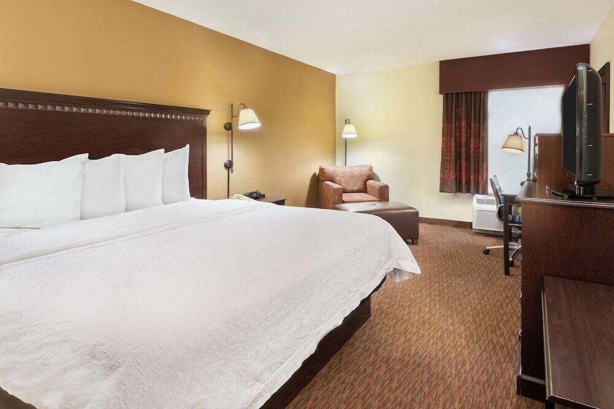 A hotel room with a large bed, a desk with a computer, a chair, and two lamps.
