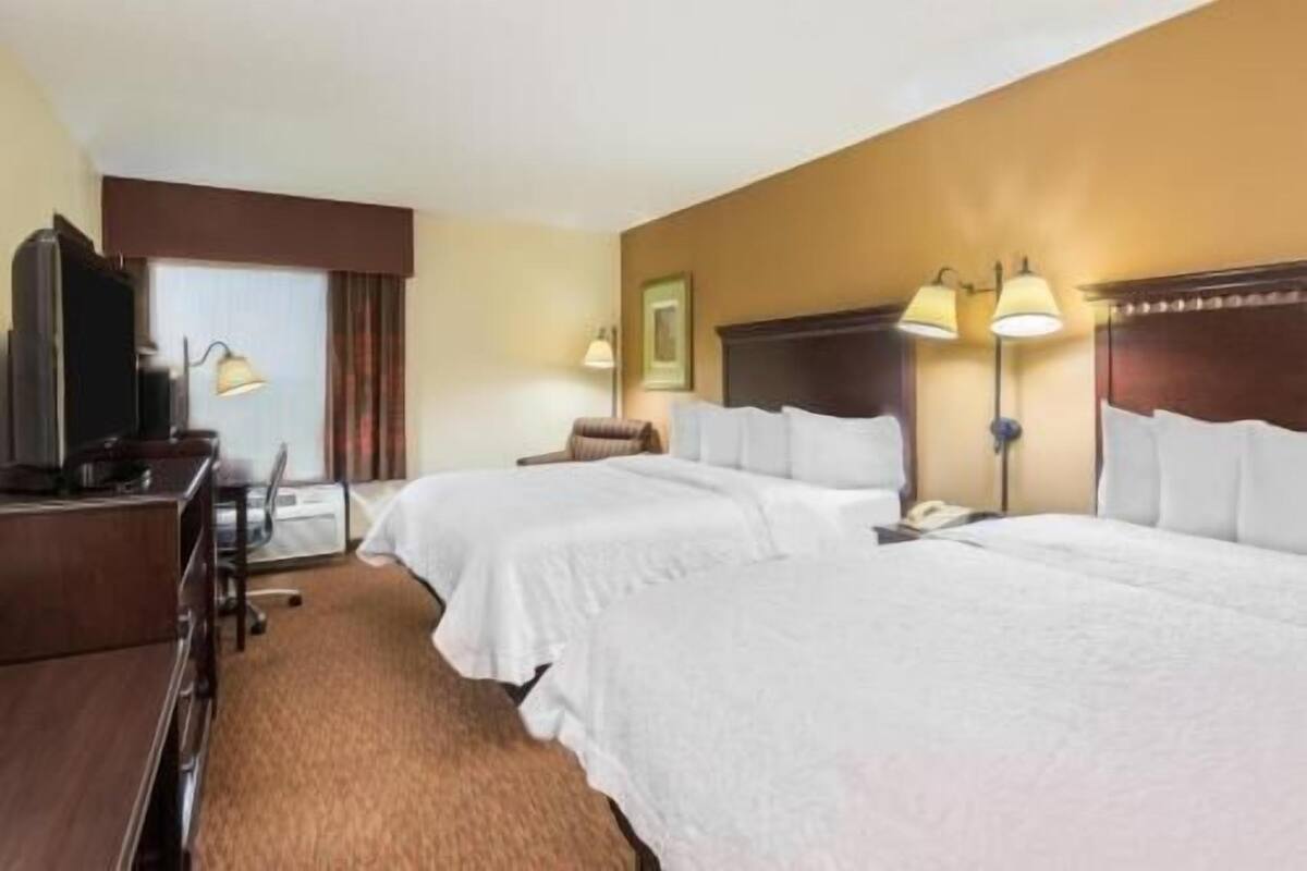 A hotel room with two beds, a desk with a lamp, a television, and a wall-mounted telephone.