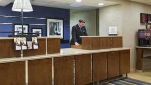 A reception desk with a blue wall, framed pictures, and a sign for 'Hospitality Honors'. - Hampton Inn Charlotte - University Place (Charlotte)