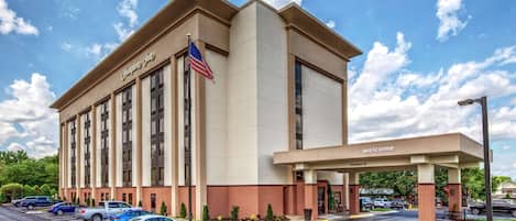 Et Hampton Inn hotel med parkeringsplads, amerikansk flag og en 'Welcome'-skilt.