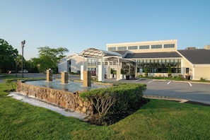 A building with a water feature in front, a parking lot, and a clear sky.