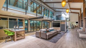 A spacious, modern interior with a high ceiling, a seating area with sofas, a desk with a computer, and a large TV screen.