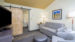 A hotel room with a gray sofa, a television on a stand, a sliding door, a framed picture on the wall, and a lamp on a side table. - Holiday Inn Hyannis by IHG (Hyannis)