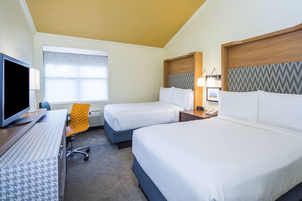 A hotel room with two beds, a desk with a computer, a chair, and a window with curtains.