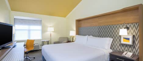A hotel room with a bed, bedside tables, a desk with a computer, a chair, and a window with blinds.