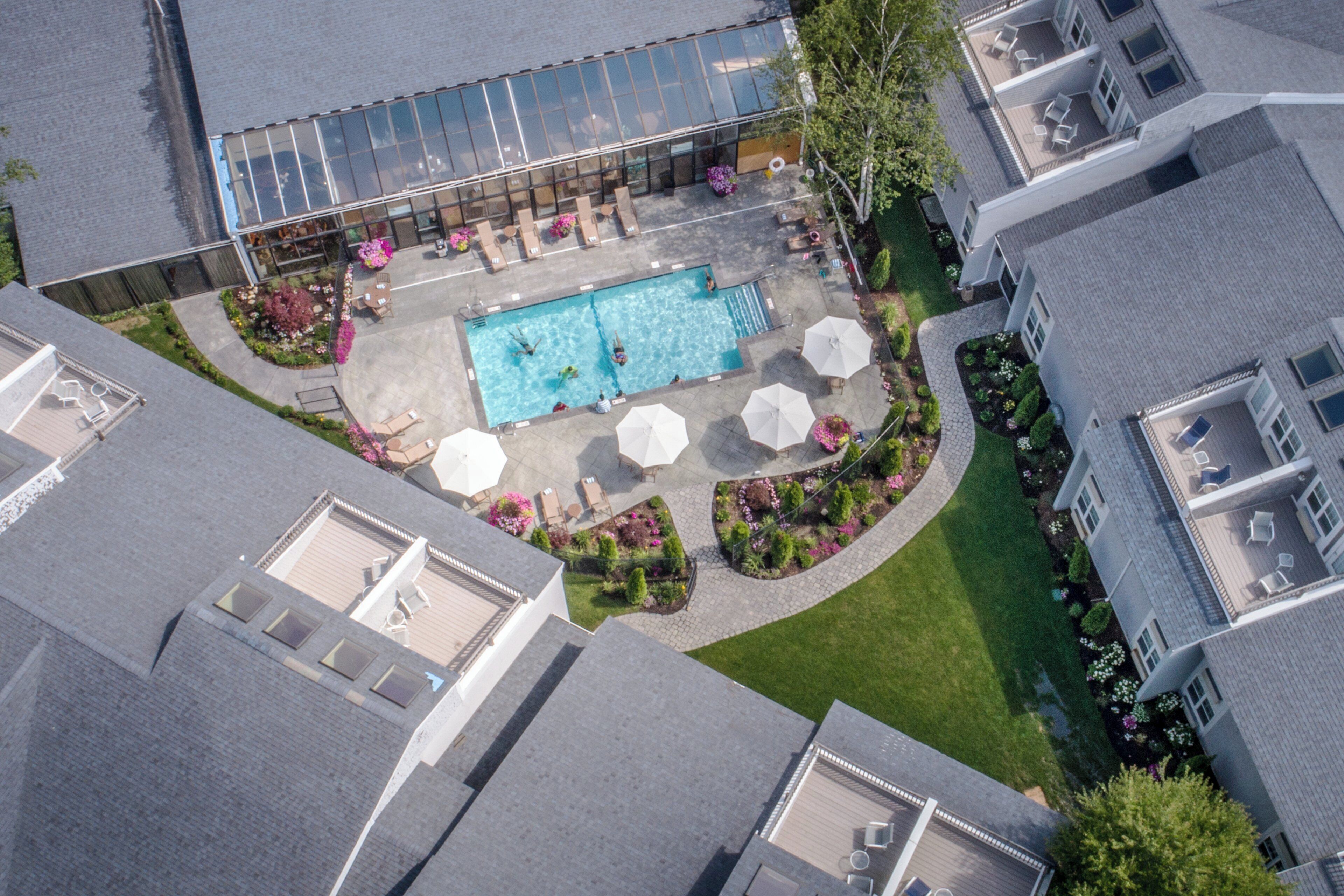 An aerial view of a residential area with a swimming pool surrounded by outdoor seating and a garden.
