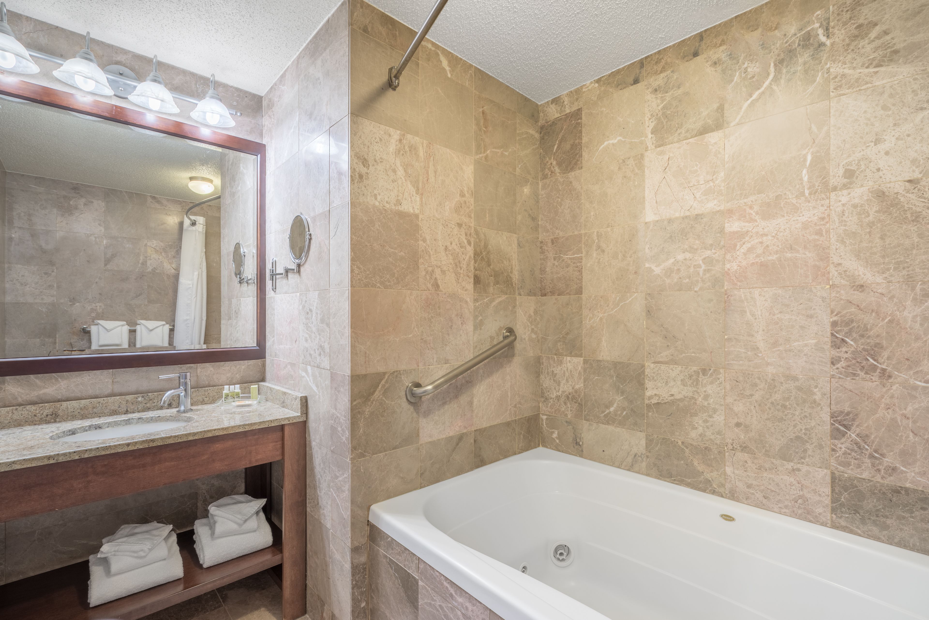 A bathroom with a marble-tiled shower, a white bathtub, a vanity with a mirror, and a towel rack.