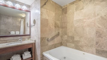 A bathroom with a marble-tiled shower, a white bathtub, a vanity with a mirror, and a towel rack.
