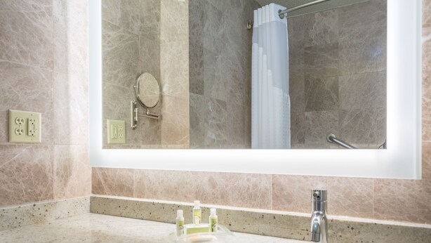 A bathroom with a large mirror, a sink, and a shower area. - Holiday Inn Hyannis by IHG (Hyannis)