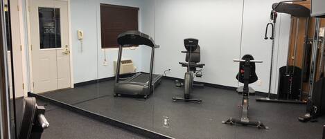 Un gimnasio con cinta de correr, bicicleta estática y máquina de pesas.