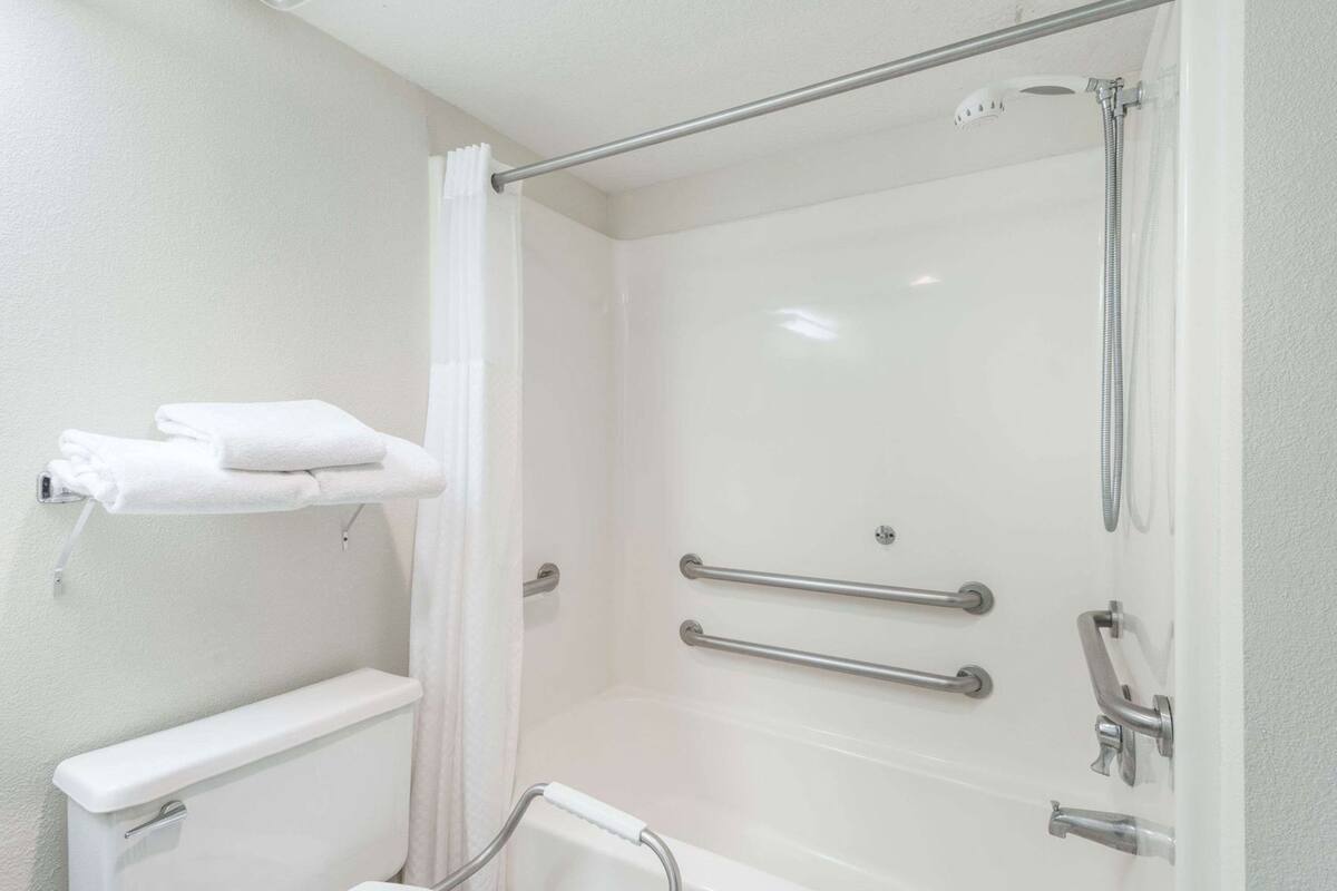 Une salle de bain équipée d’une douche, de barres d’appui, d’un porte-serviettes et de toilettes.