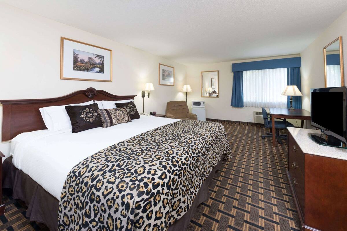 Une chambre d’hôtel avec un grand lit, un bureau, une télévision et une fenêtre avec des rideaux.