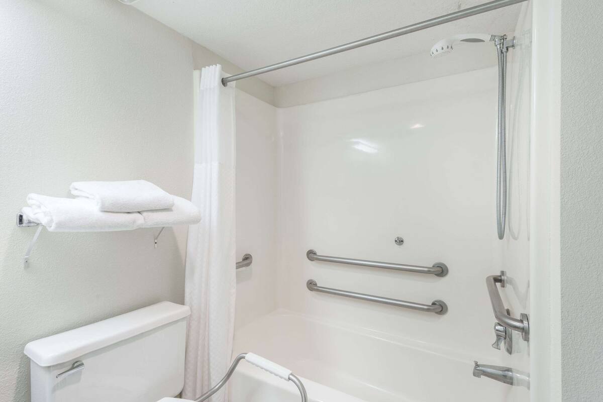 Une salle de bain avec une baignoire blanche, une douche équipée d’un pommeau de douche amovible et des toilettes dotées d’une barre d’appui.