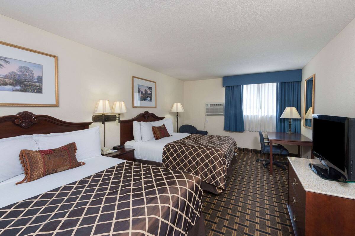 Une chambre d’hôtel avec deux lits, un bureau, une télévision et une fenêtre avec des rideaux.