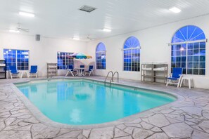 An indoor swimming pool with stone flooring, blue chairs, and large arched windows. - Baymont by Wyndham Osage Beach (Osage Beach)