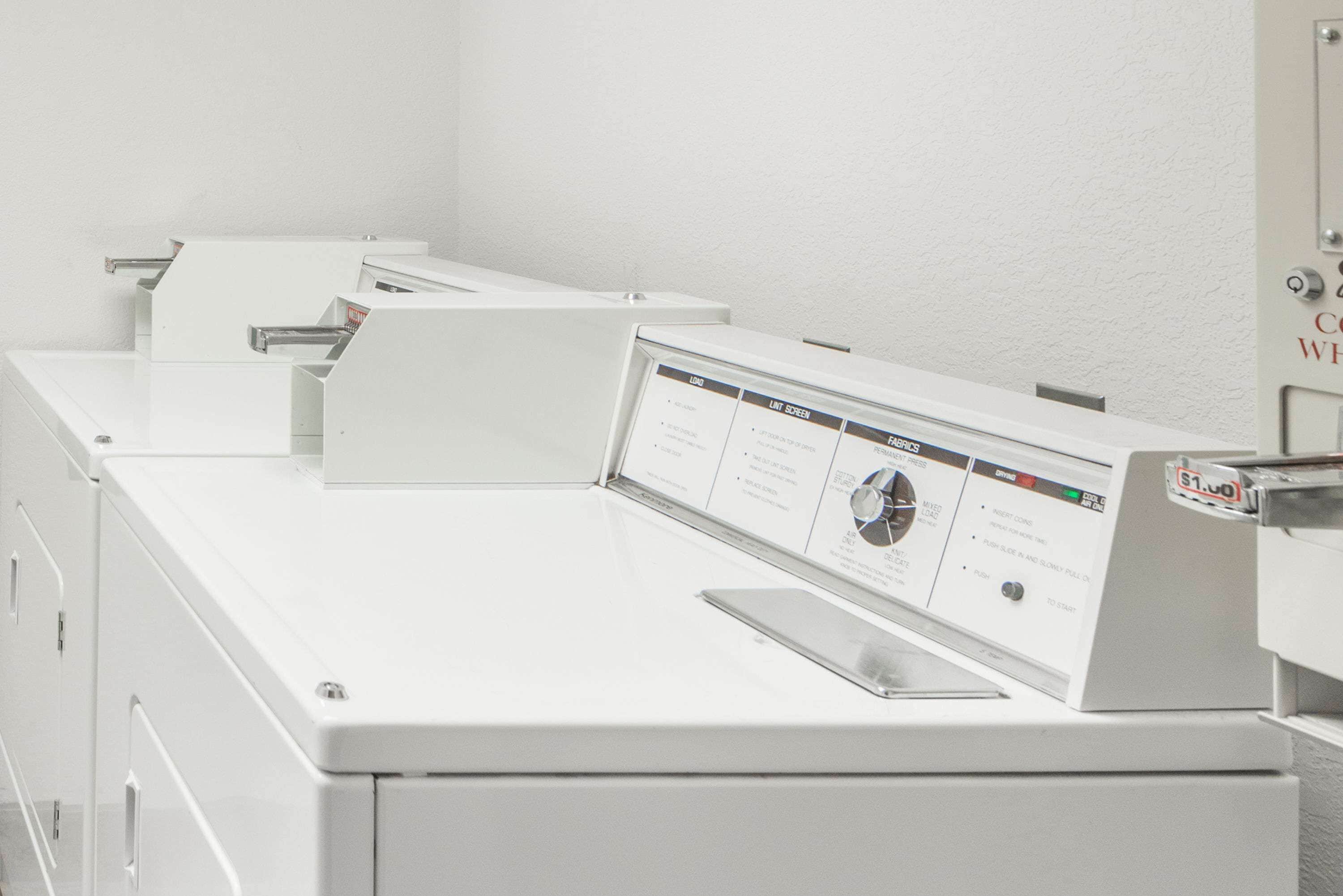 A row of white laundry machines with control panels displaying various settings.