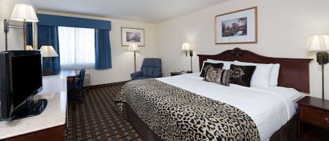A hotel room with a large bed, a desk with a computer, a chair, and two lamps.