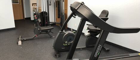 A gym with a treadmill, weight machines, and a bench.