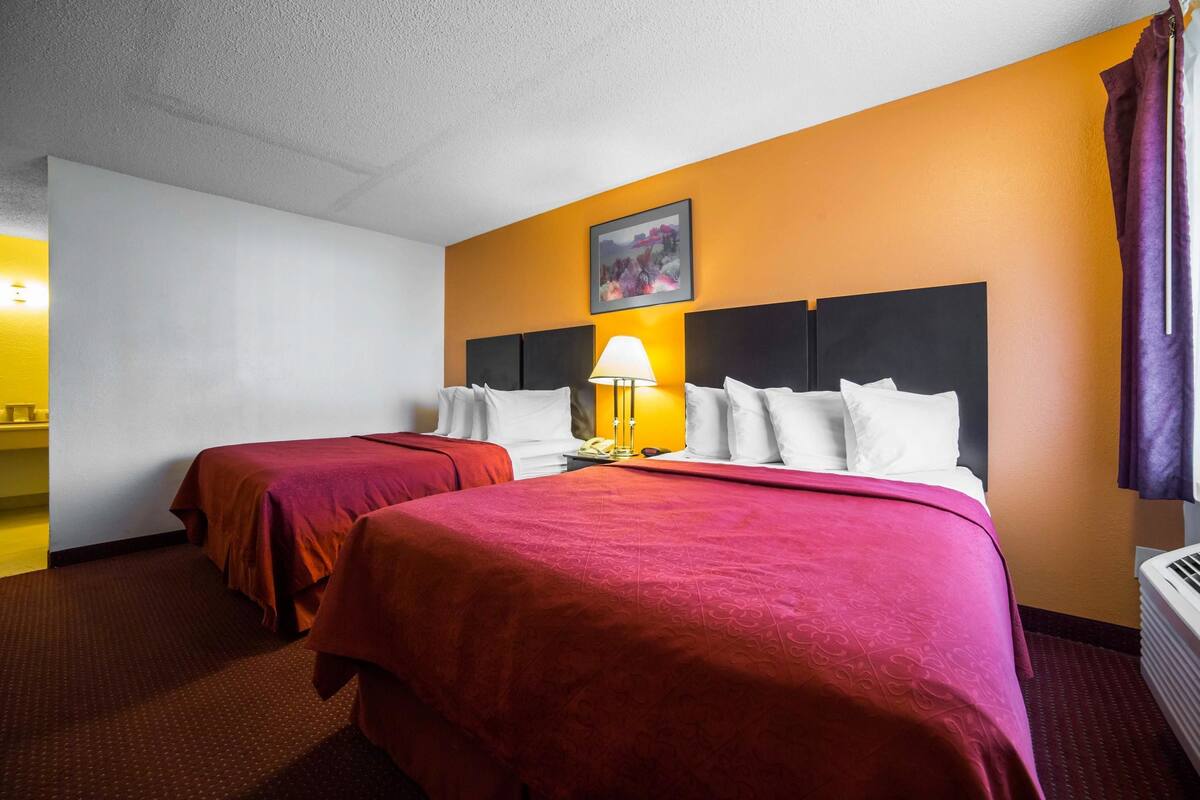 A hotel room with two beds, a nightstand with a lamp, and a painting on the wall.