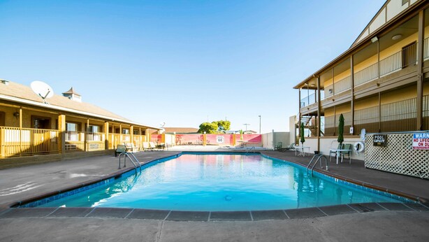 Une piscine dotée d’un poste de surveillance pour les sauveteurs, d’un panneau indiquant la capacité maximale de la piscine, et d’un bâtiment avec des balcons et une antenne parabolique.