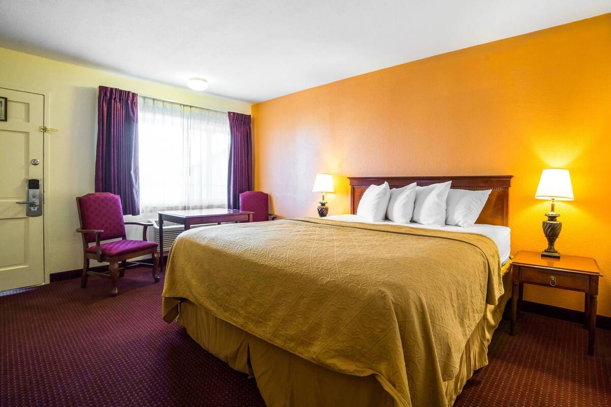 A hotel room with a large bed, two bedside lamps, a desk, and a chair.