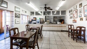 Un restaurant avec des tables et des chaises en bois, un espace cuisine et divers tableaux encadrés accrochés aux murs.