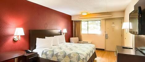 Habitación de hotel con cama, lámparas de noche, escritorio, silla, televisor y ventana con cortinas.