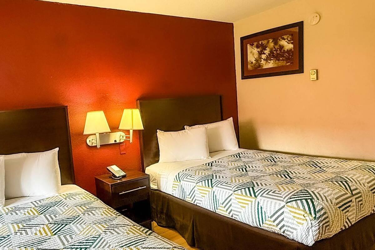 A hotel room with two beds, each with a patterned bedspread and white pillows. There are two bedside lamps and a nightstand with a phone.