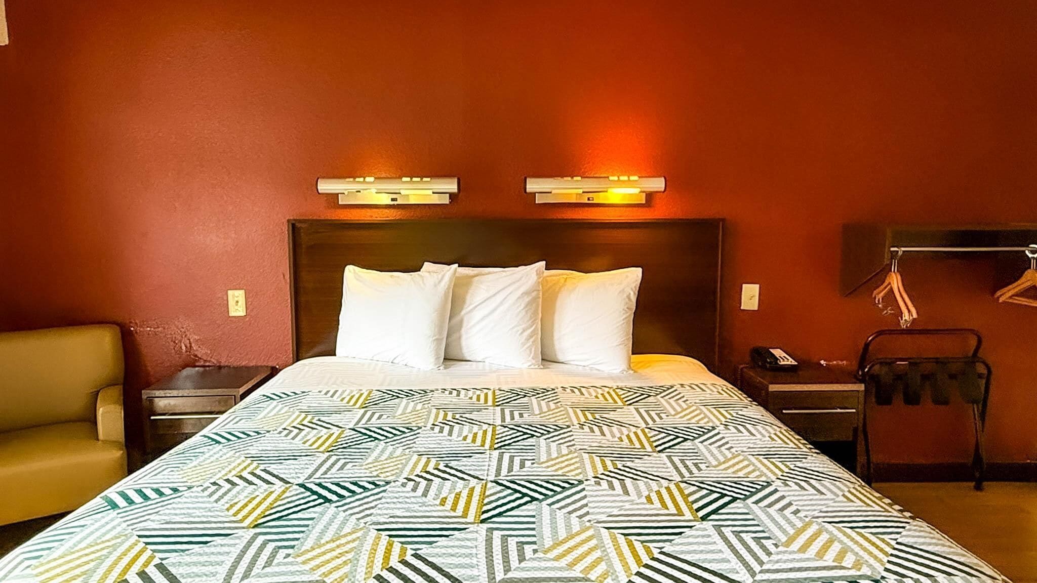 A hotel room with a large bed, two bedside tables, a chair, and a coat rack.