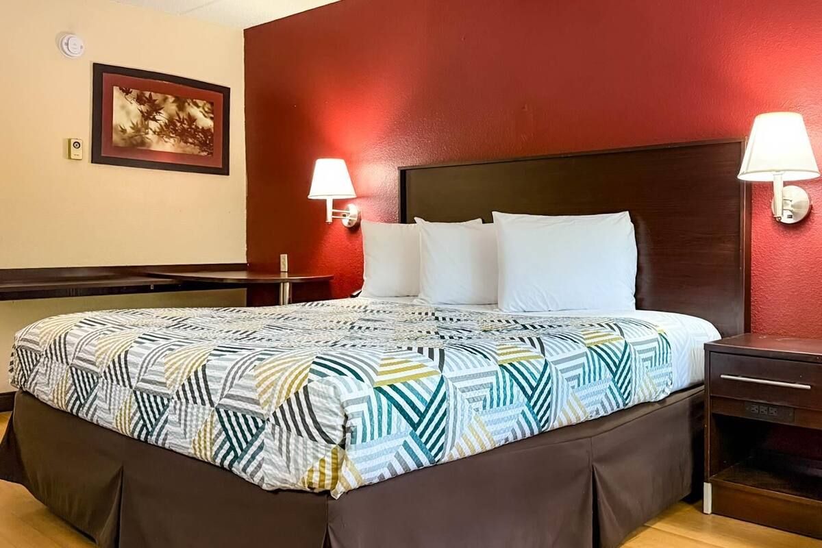 A hotel room with a large bed, two bedside lamps, a nightstand, a chair, and a small table.