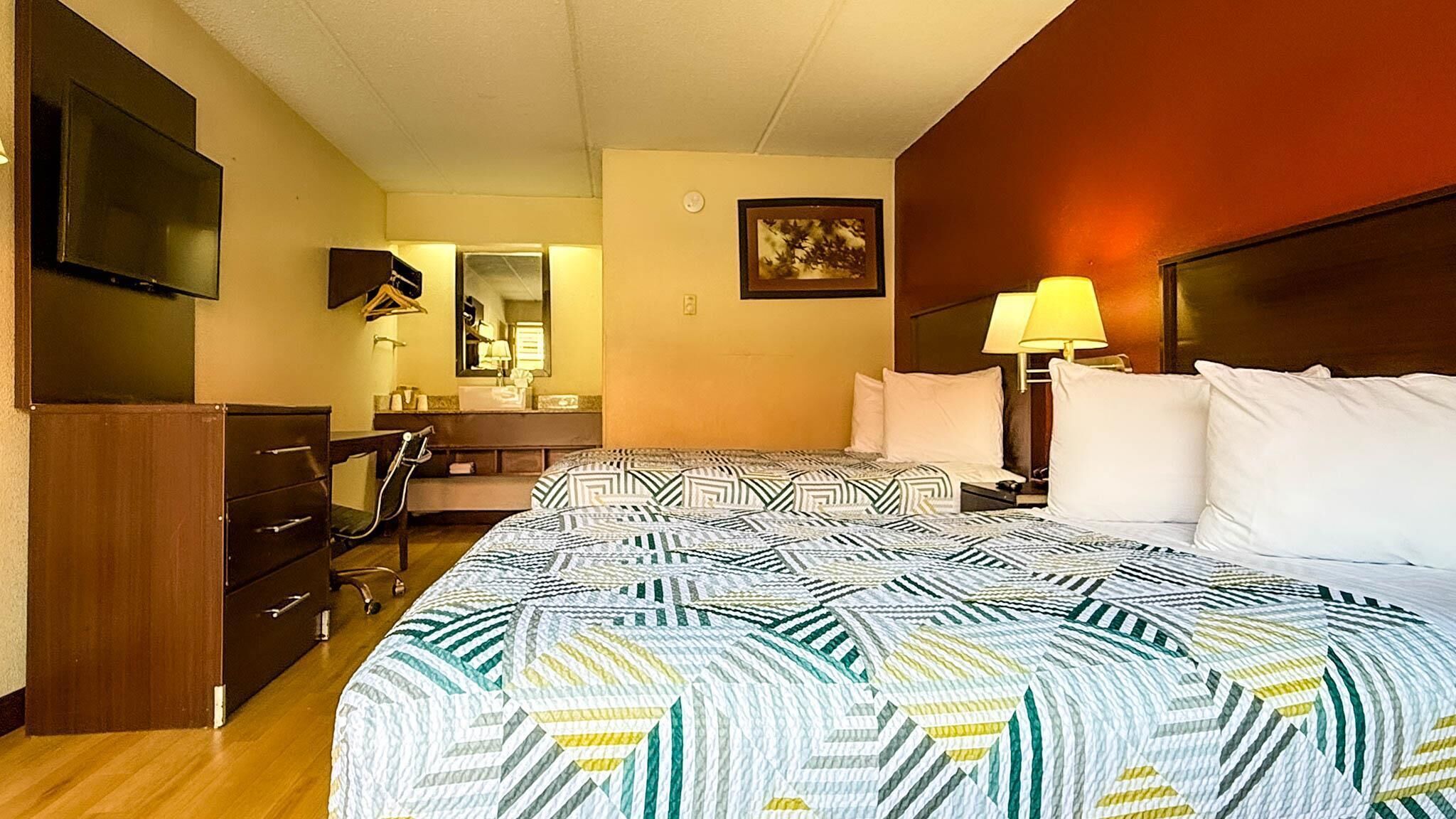 Habitación de hotel con una cama grande, un escritorio, una silla, un aparador, un televisor y una lámpara.
