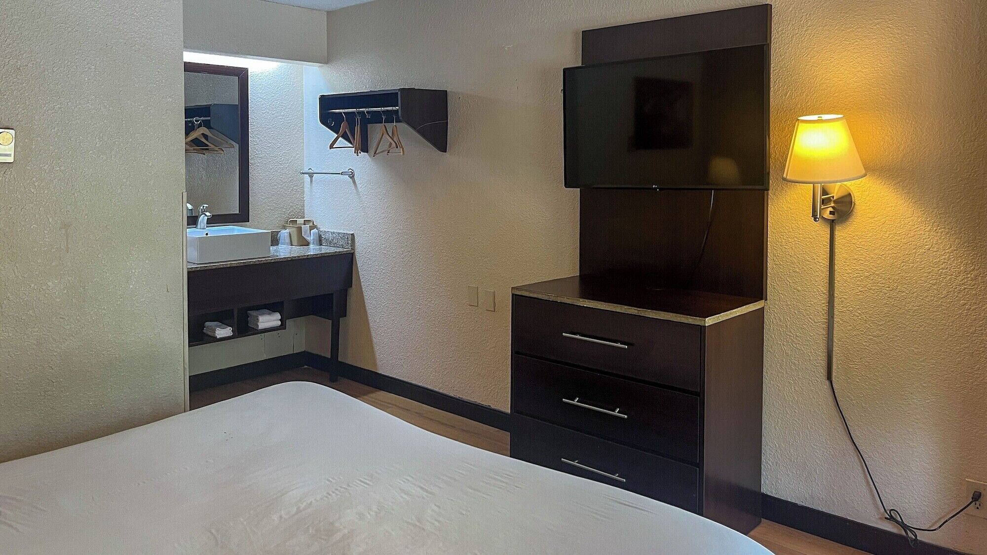 Une chambre d’hôtel avec un lit, une coiffeuse avec un miroir, une télévision et une lampe.