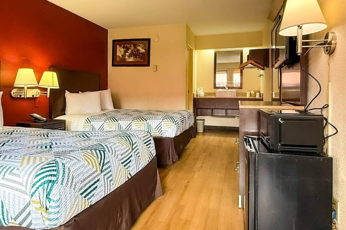 A hotel room with two beds, a desk, a TV, and a bathroom visible in the background.
