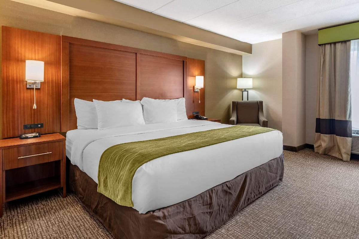 A hotel room with a large bed, wooden headboard, bedside lamps, a desk, and a chair.