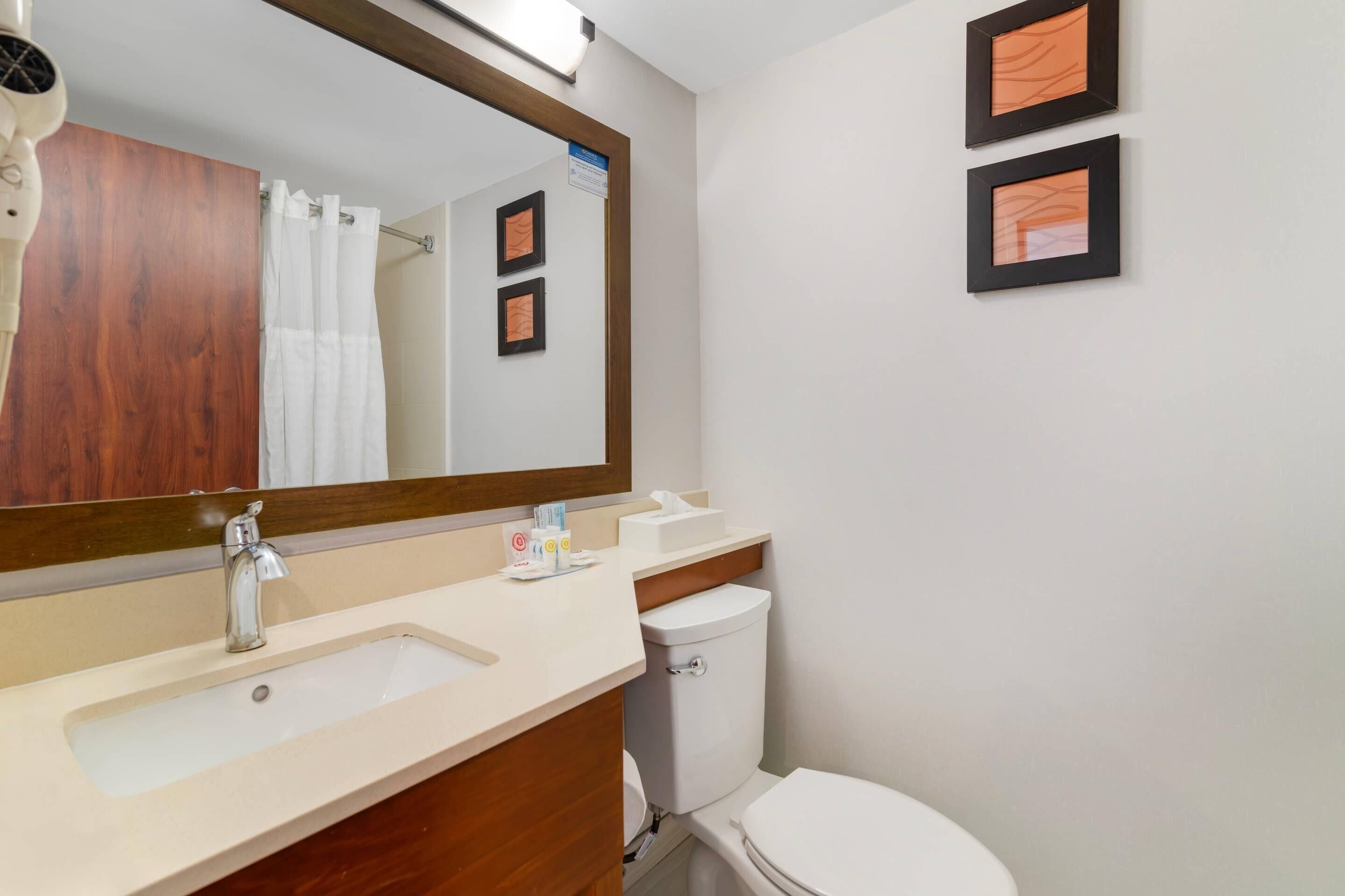 A bathroom with a sink, mirror, toilet, and framed pictures on the wall.