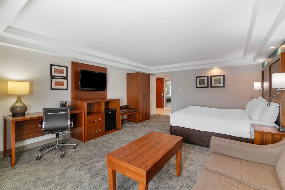 A hotel room with a bed, desk, chair, TV, wardrobe, and a small table.